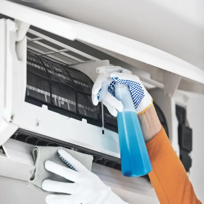 Person cleaning air conditioner filter with spray bottle and cloth