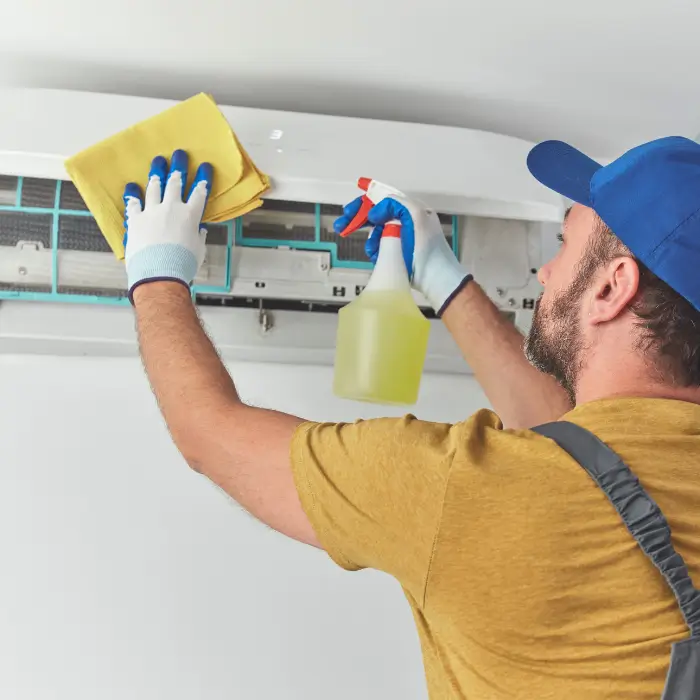 Technician cleaning air conditioner with spray and cloth