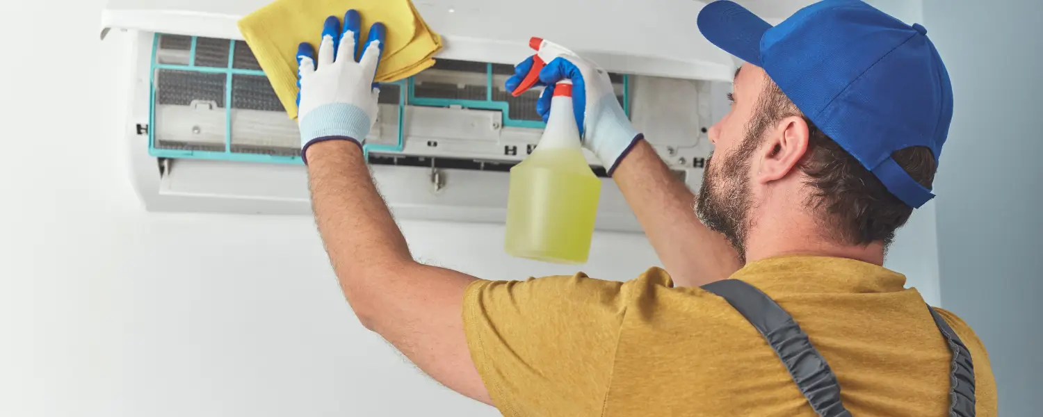 Technician cleaning air conditioner with spray and cloth