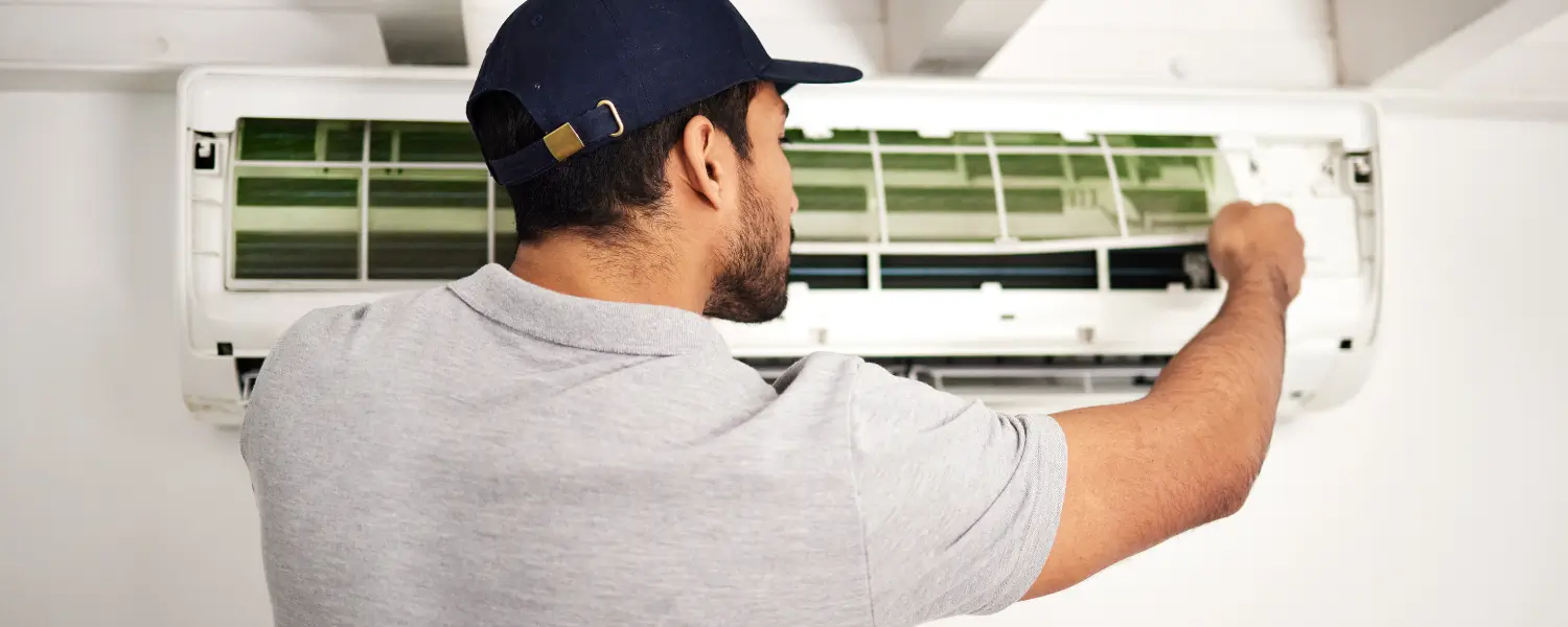 Man servicing wall-mounted air conditioner with opened front panel
