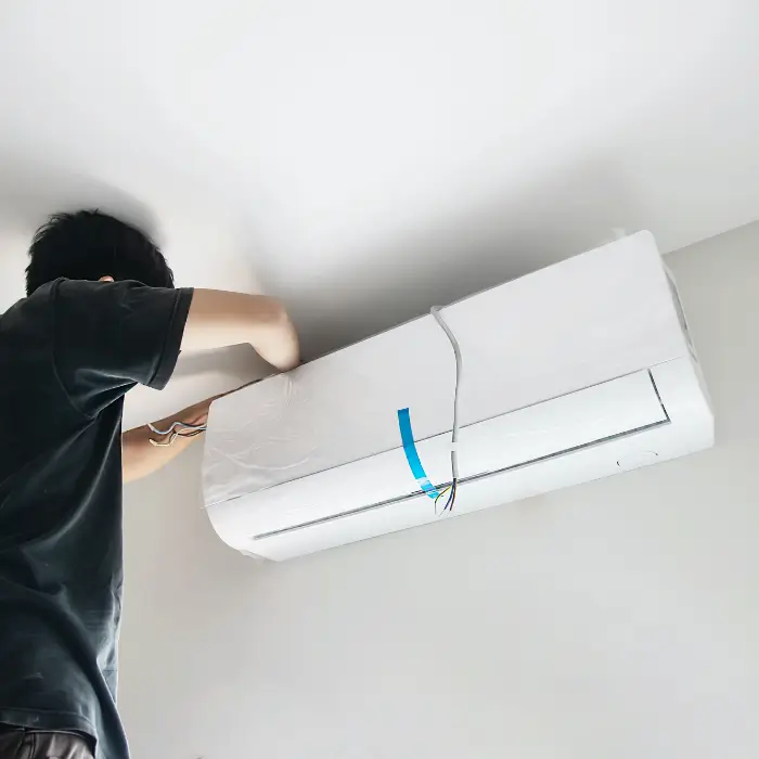 Technician installing or repairing wall-mounted air conditioner with exposed wiring