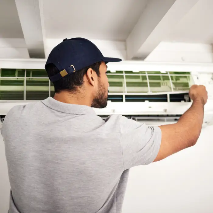 Man servicing wall-mounted air conditioner with opened front panel